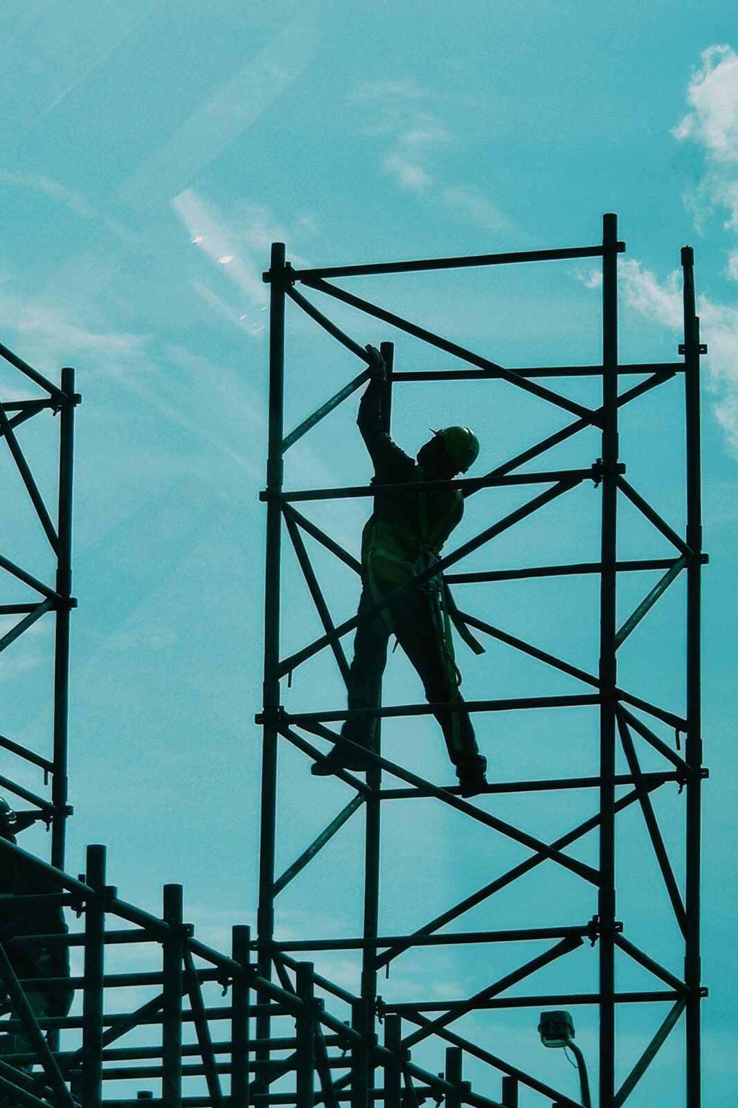 Bauarbeiter sichert sich an einem mehrstöckigen Stahlgerüst gegen den Himmel
